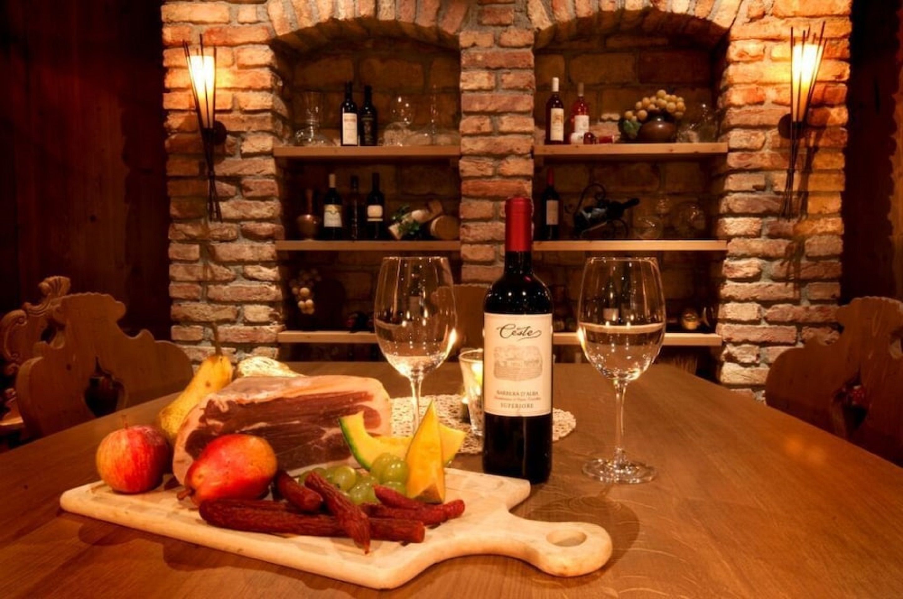 Una mesa de madera con una botella de vino, copas y una bandeja de frutas.