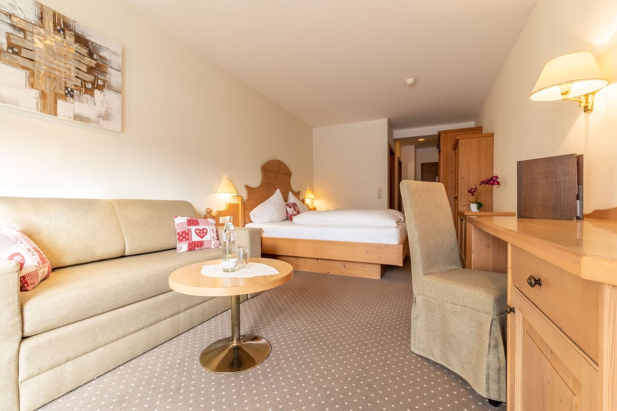 Une chambre d’hôtel confortable, avec un lit, un canapé, un fauteuil, une petite table et une armoire en bois.