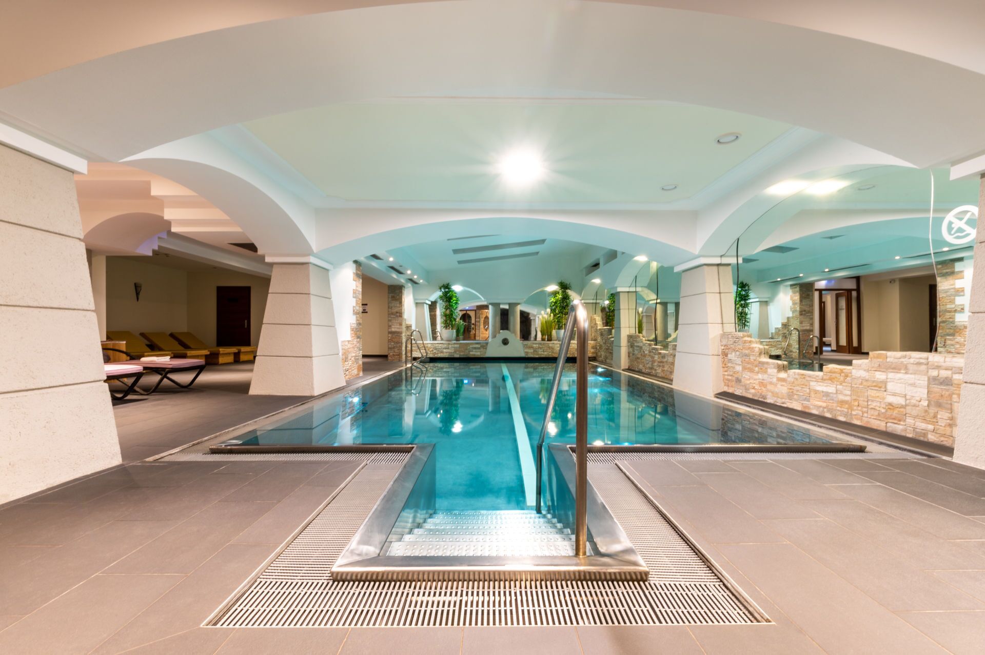 Una piscina interior con agua cristalina, rodeada de muros de piedra y suelo de baldosas.