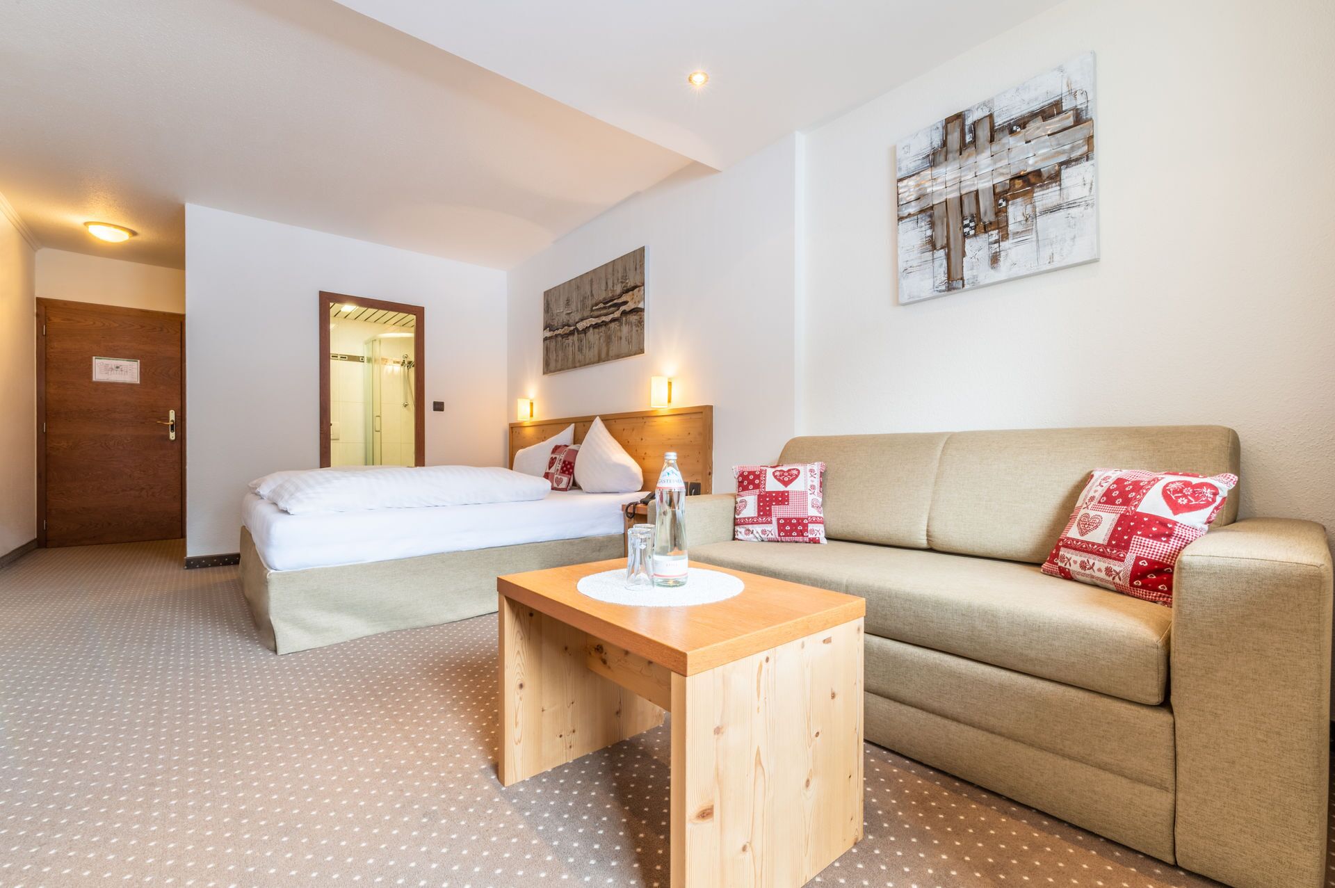 Habitación de hotel con cama, sofá, mesita de madera y un cuadro colgado en la pared.