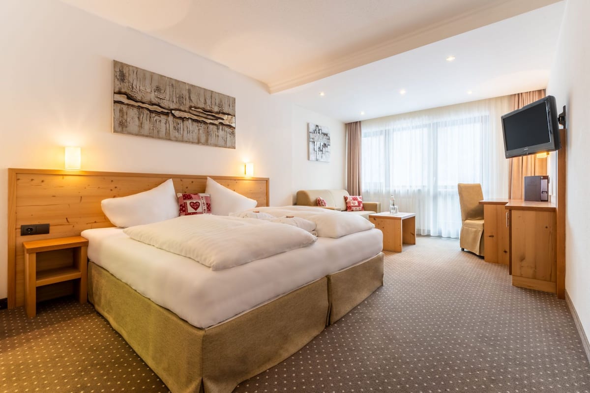 Une chambre d’hôtel avec un grand lit, un bureau, une télévision et une fenêtre avec des rideaux.