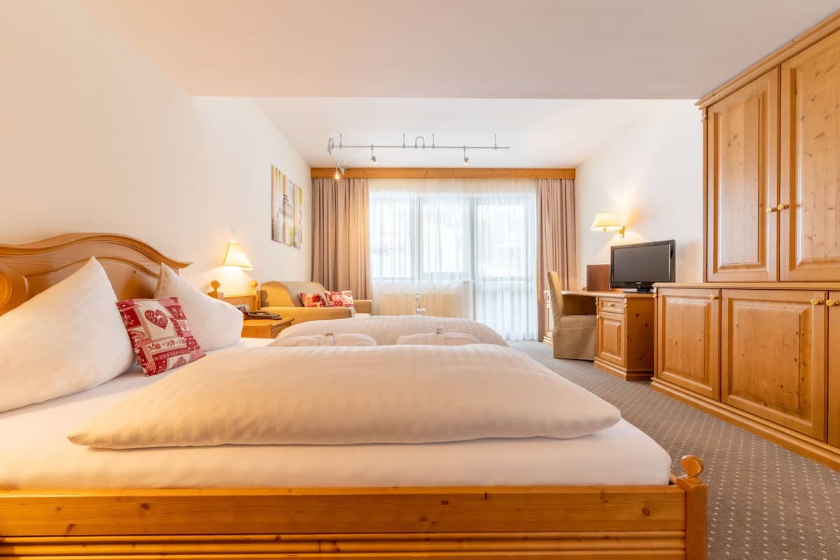 Une chambre d’hôtel avec un grand lit, un bureau avec une télévision et des meubles en bois.