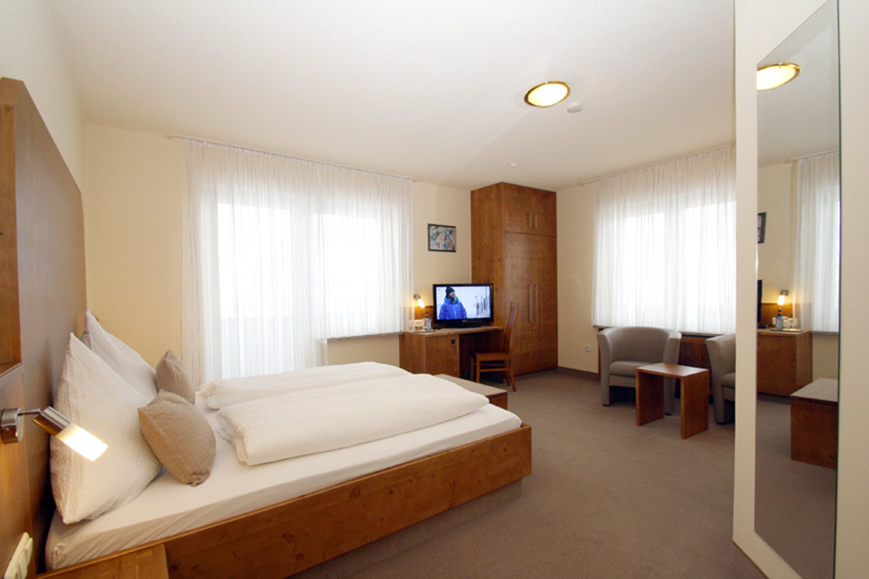 A hotel room with a large bed, a television, a desk with a chair, and a mirror.