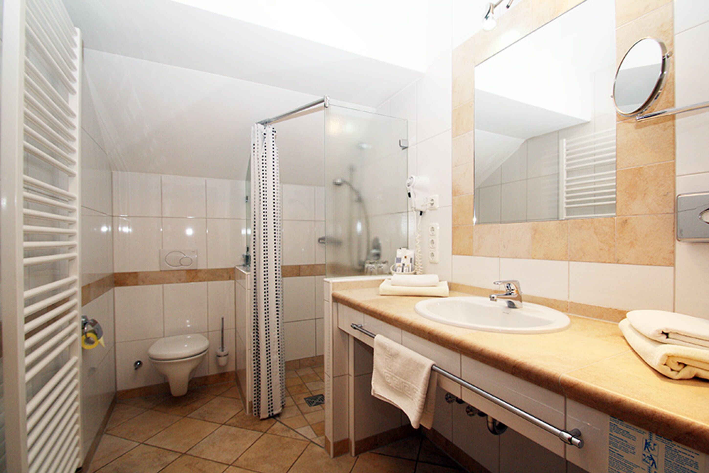 Un baño moderno con cabina de ducha de vidrio, inodoro, lavamanos con tocador y un espejo grande.
