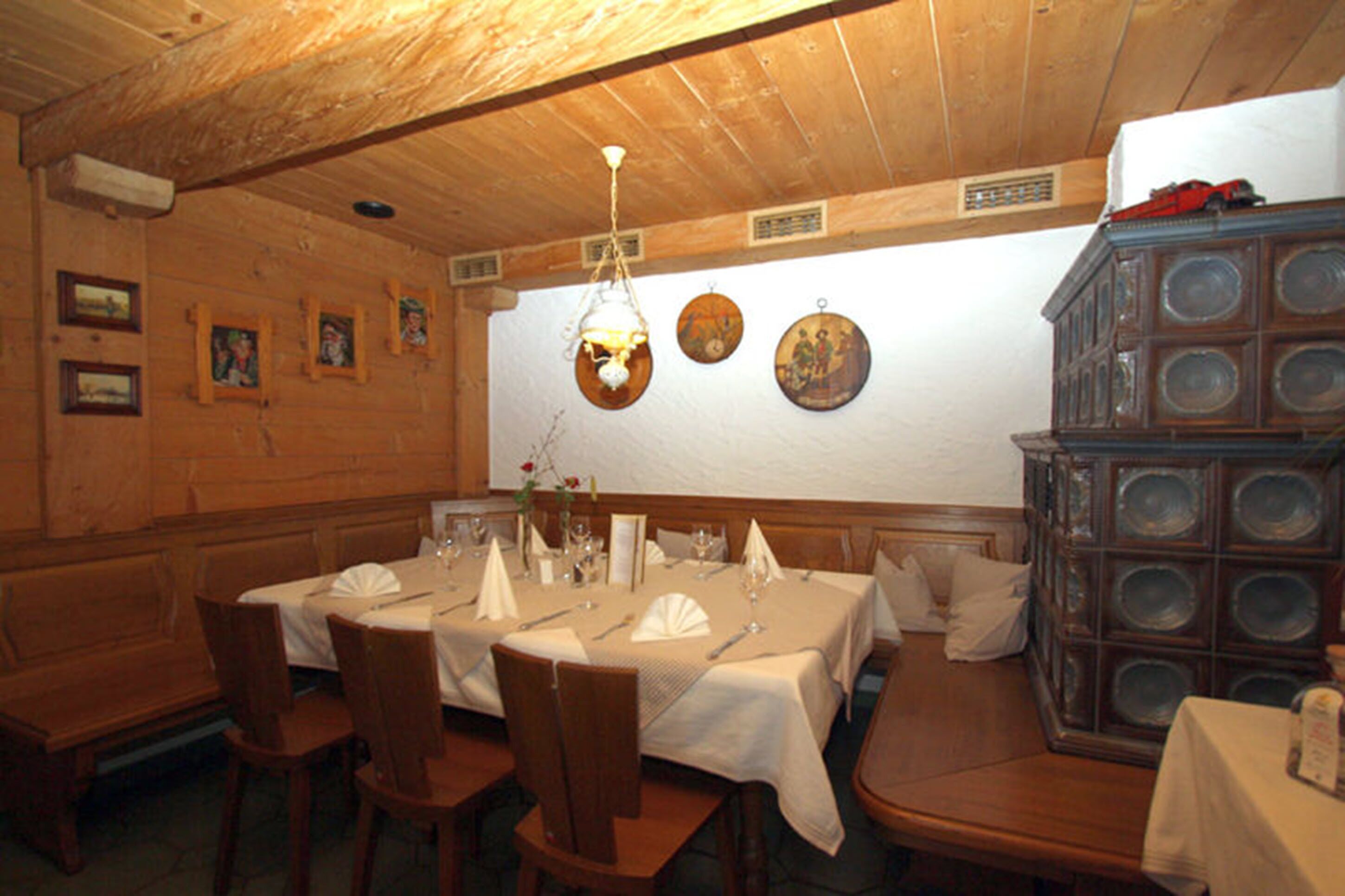 A dining area with wooden walls, a high ceiling, and a chandelier. Tables are set with white tablecloths and chairs.