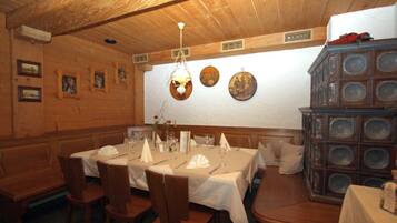A dining area with wooden walls, a high ceiling, and a chandelier. Tables are set with white tablecloths and chairs.