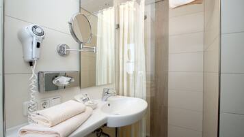 Een badkamer met een wit wastafel, een haardroger, een spiegel en een douchegordijn.