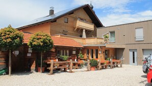 A wooden building with a balcony, outdoor seating, and a gravel ground. - Gasthaus Bonimeier (Haiming)