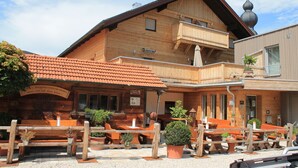 A wooden building with a balcony, outdoor seating, and potted plants. - Gasthaus Bonimeier (Haiming)