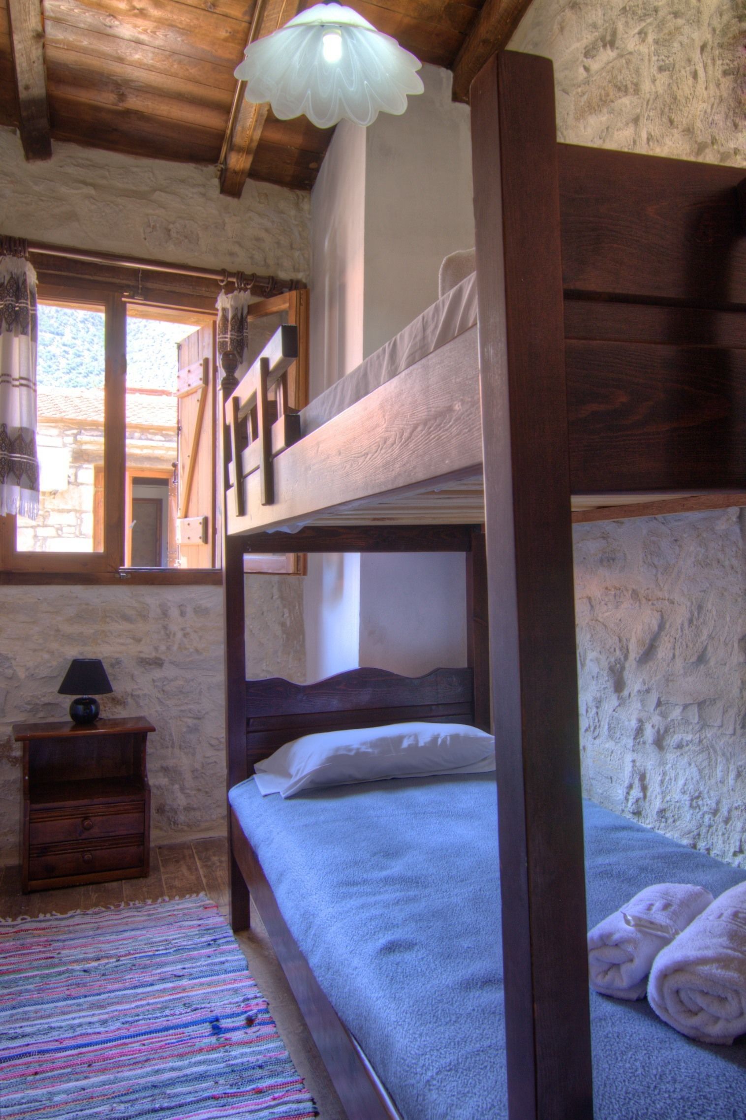 Habitación con literas, techo de madera, mesita de noche con lámpara y ventana con vista al exterior.