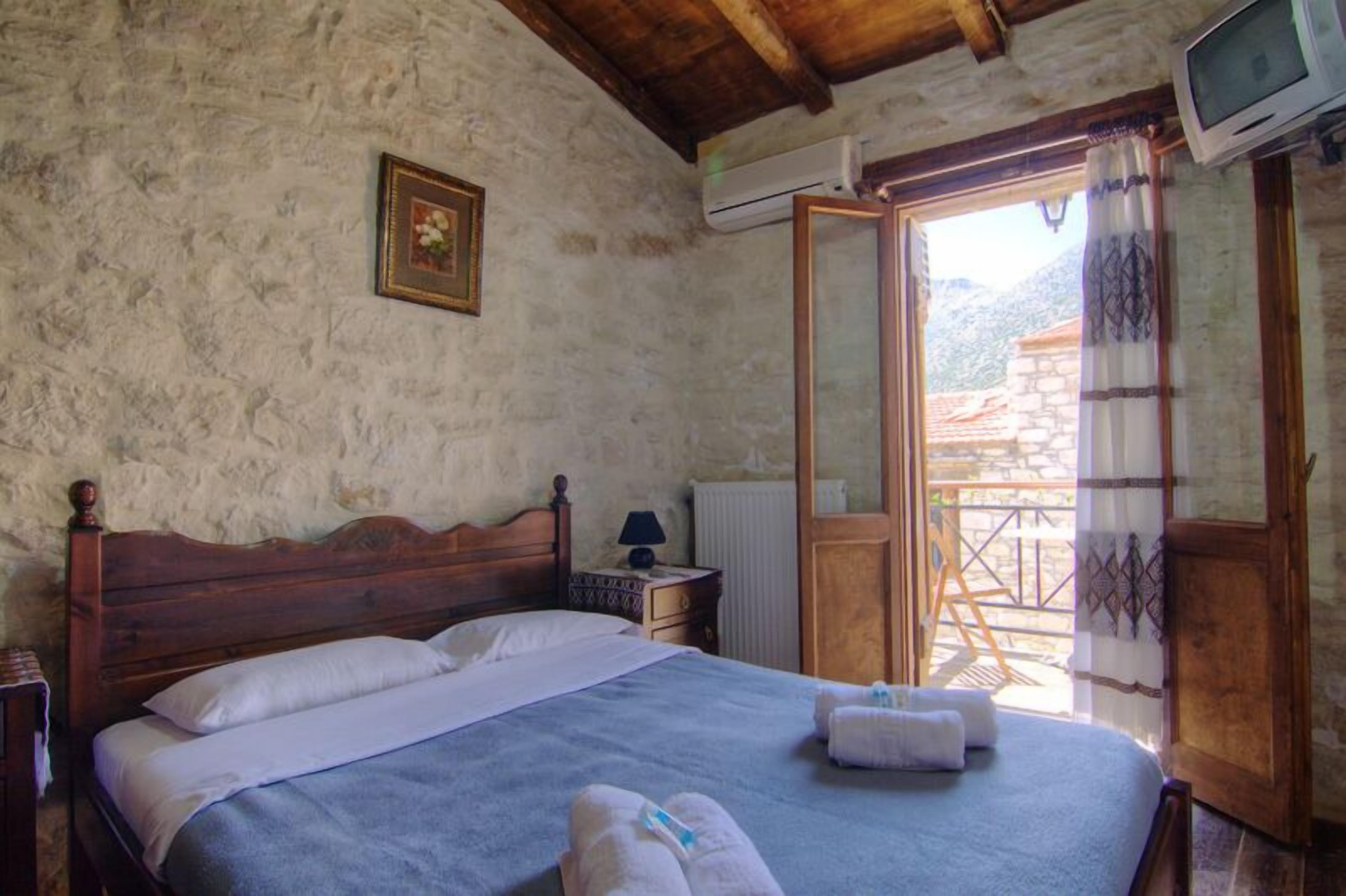 A bedroom with a wooden bed, a nightstand, a TV, and a window with a view of a mountain.