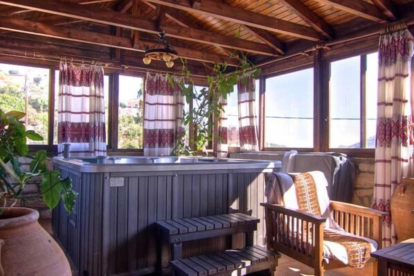 A wooden deck with a hot tub, wooden benches, and a chair.