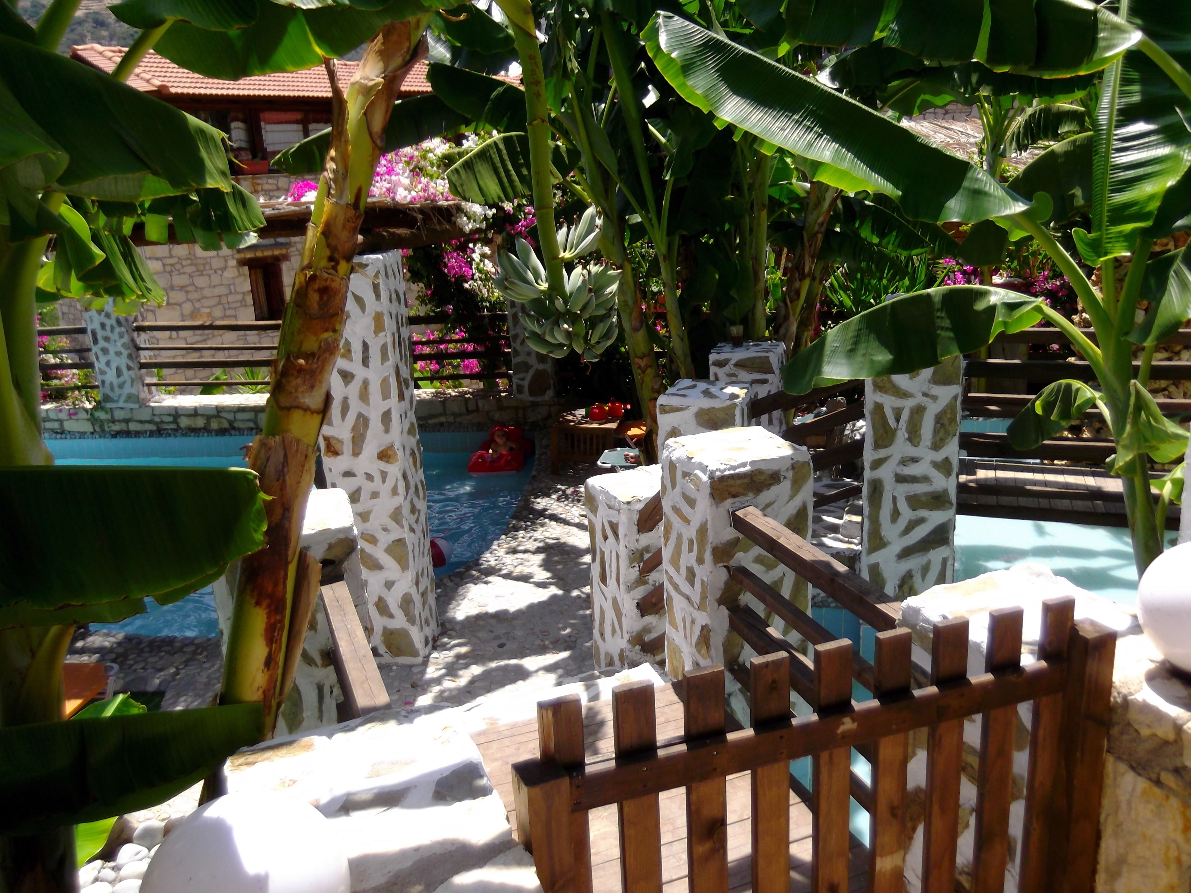 A pool area with stone pillars, wooden fence, and lush greenery.