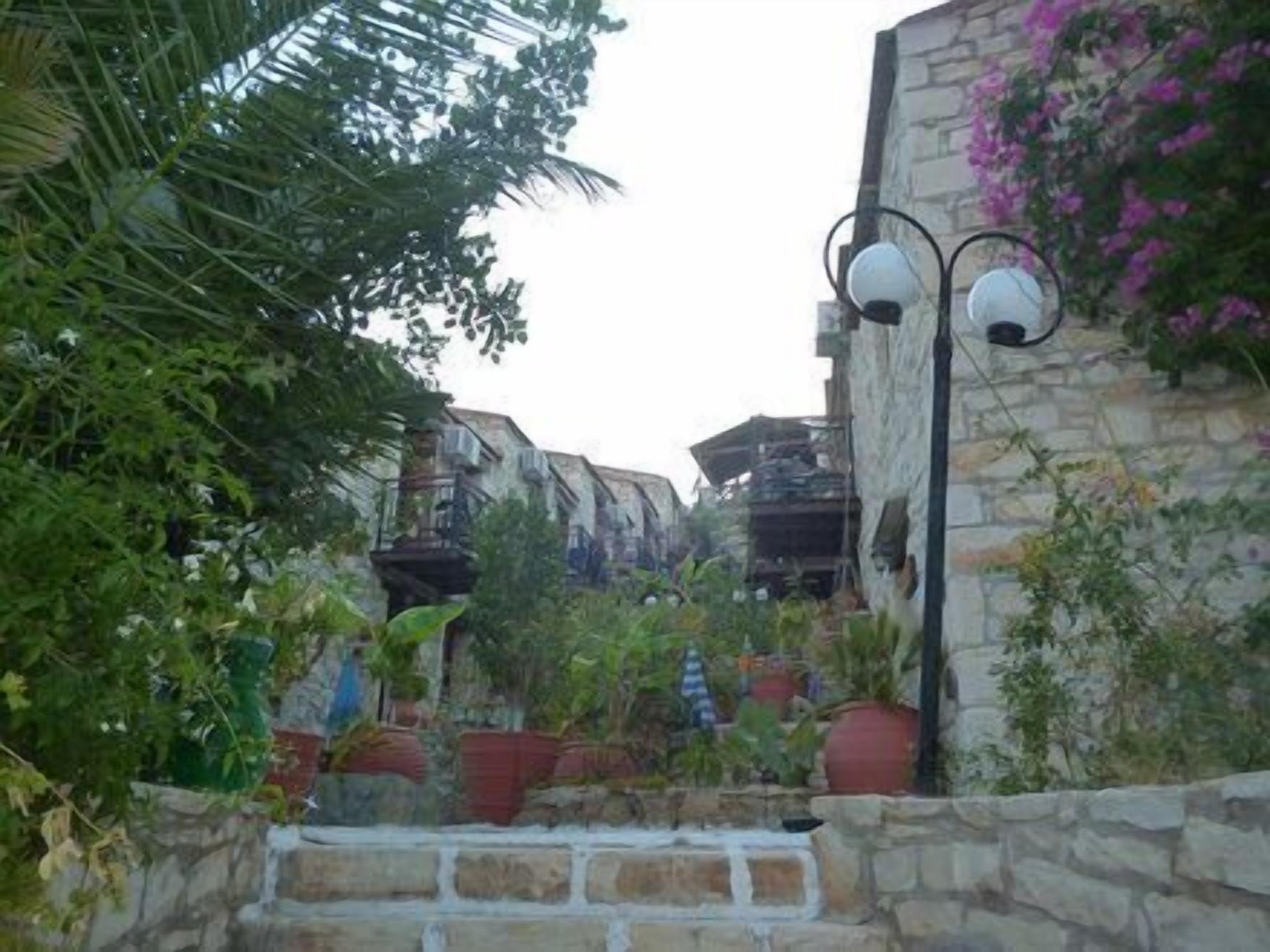 Un étroit sentier de pierre mène à un bâtiment doté de balcons, qui est entouré d’une végétation luxuriante et de plantes en pot.