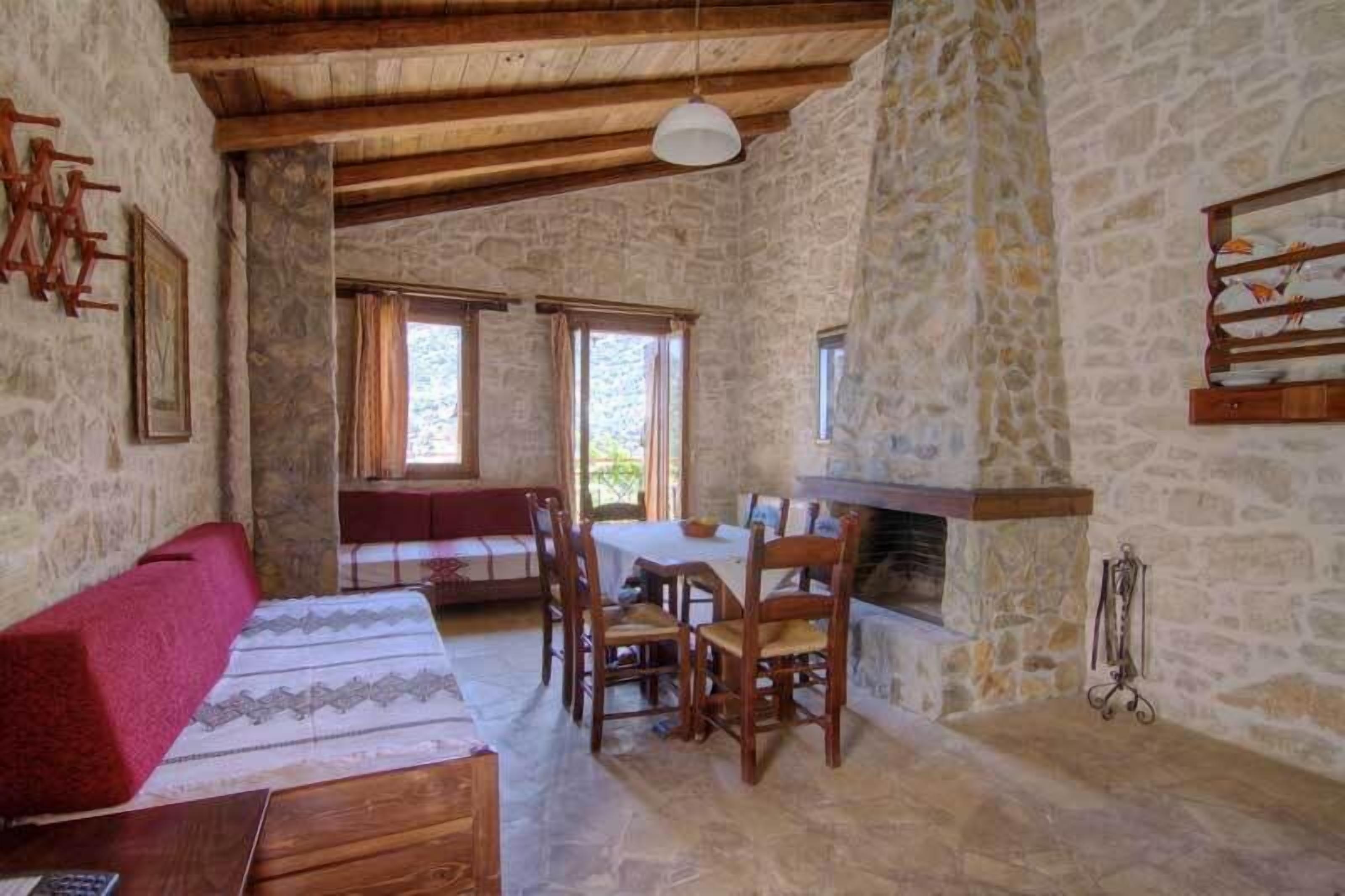 A rustic room with stone walls, a wooden ceiling, a fireplace, a dining table with chairs, and a sofa.