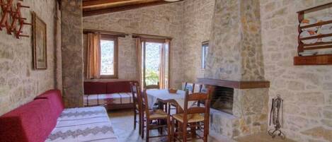 Une pièce rustique avec des murs en pierre, un plafond en bois, une cheminée, une table à manger avec des chaises et un canapé.