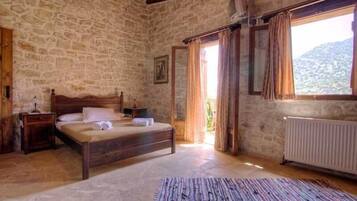 A bedroom with stone walls, a wooden bed, a radiator, and a window with curtains.