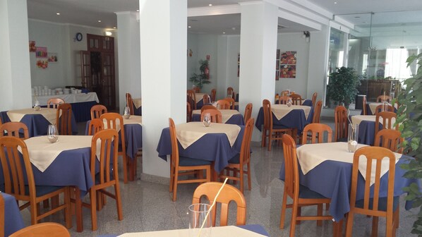 A dining area with multiple tables and chairs, each covered with a blue tablecloth. - Hotel Residencial Colibri (Almada)