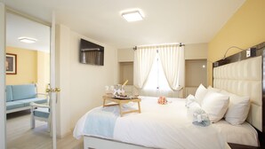 Una habitación de hotel con cama, mesita de noche, televisor y ventana con cortinas.