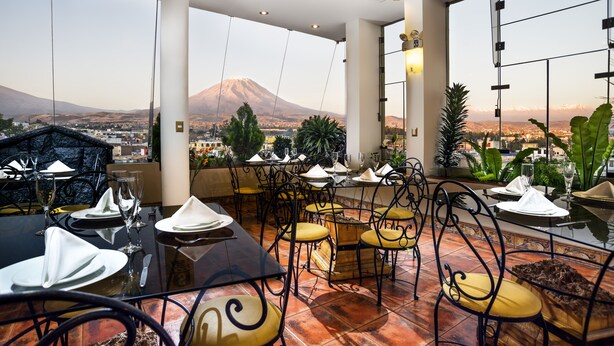 Un restaurante con terraza, mesas dispuestas para comer y vistas a una montaña.