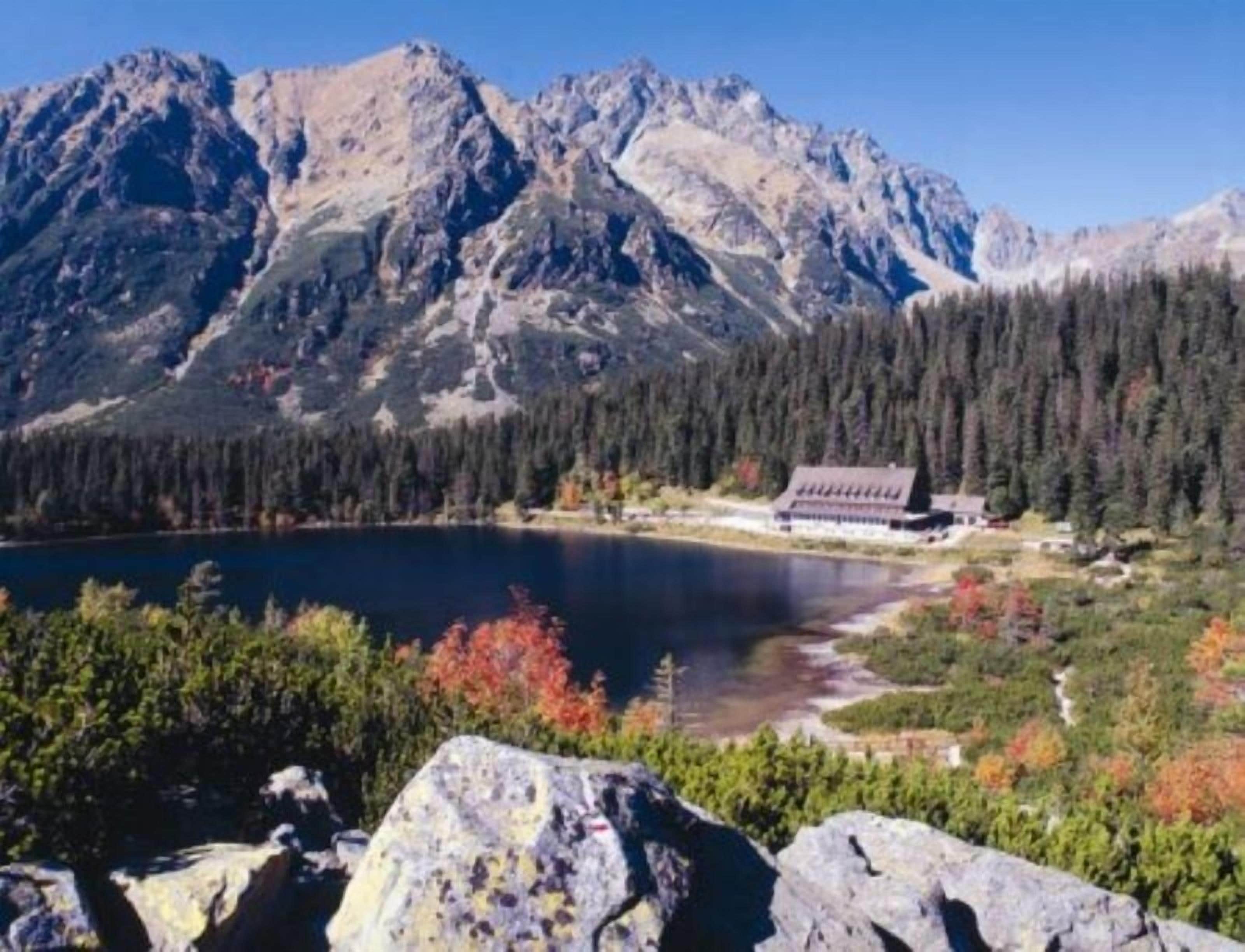 A mountain lodge with a lake view, surrounded by forest and rocky terrain.