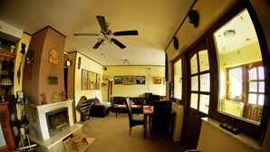 A cozy living room with a fireplace, a ceiling fan, and a dining area with a window. - Penzion Plesnivec (Poprad)