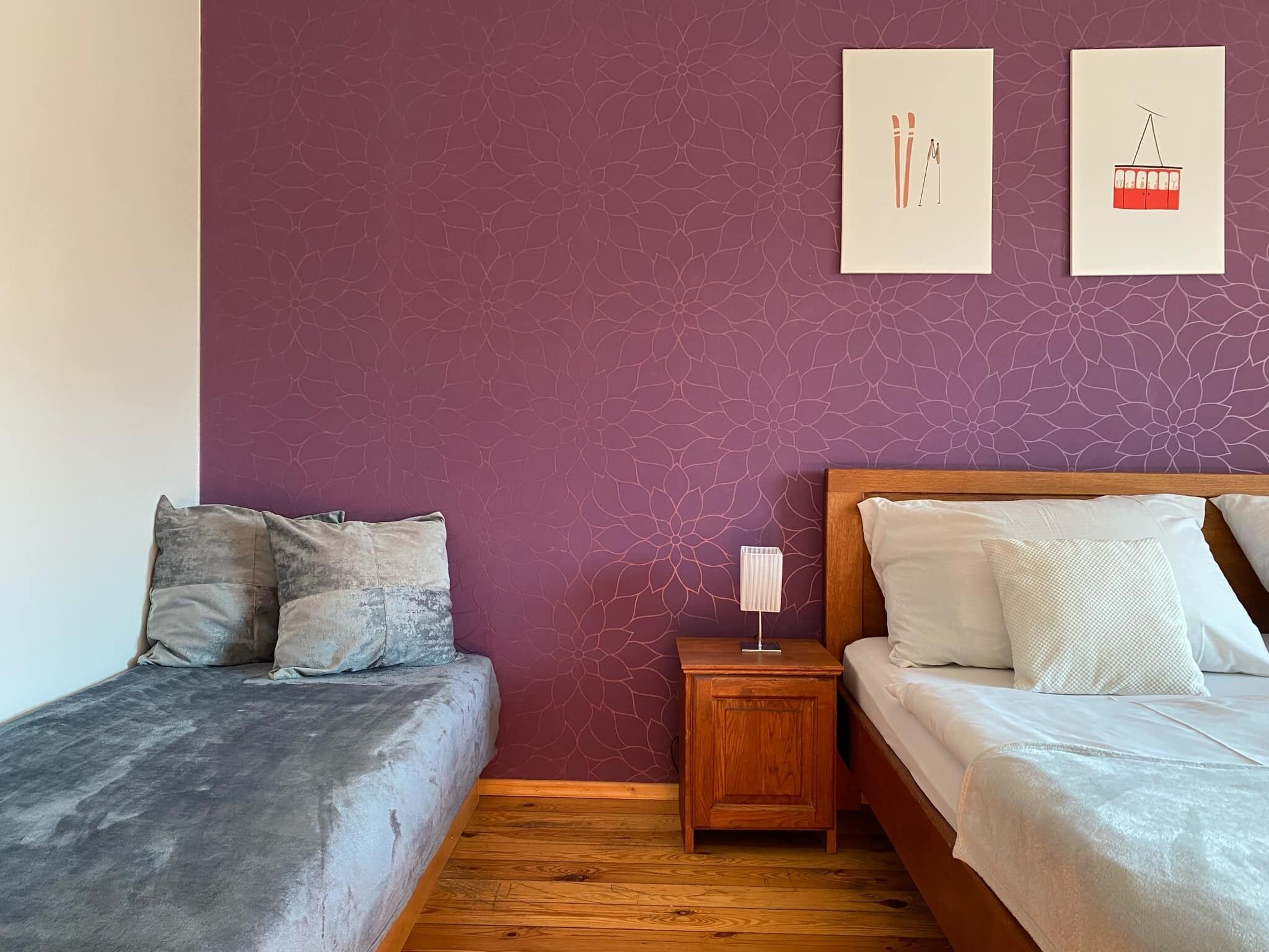 Un dormitorio con dos camas, una mesita de noche de madera y una pared con estampado floral púrpura.