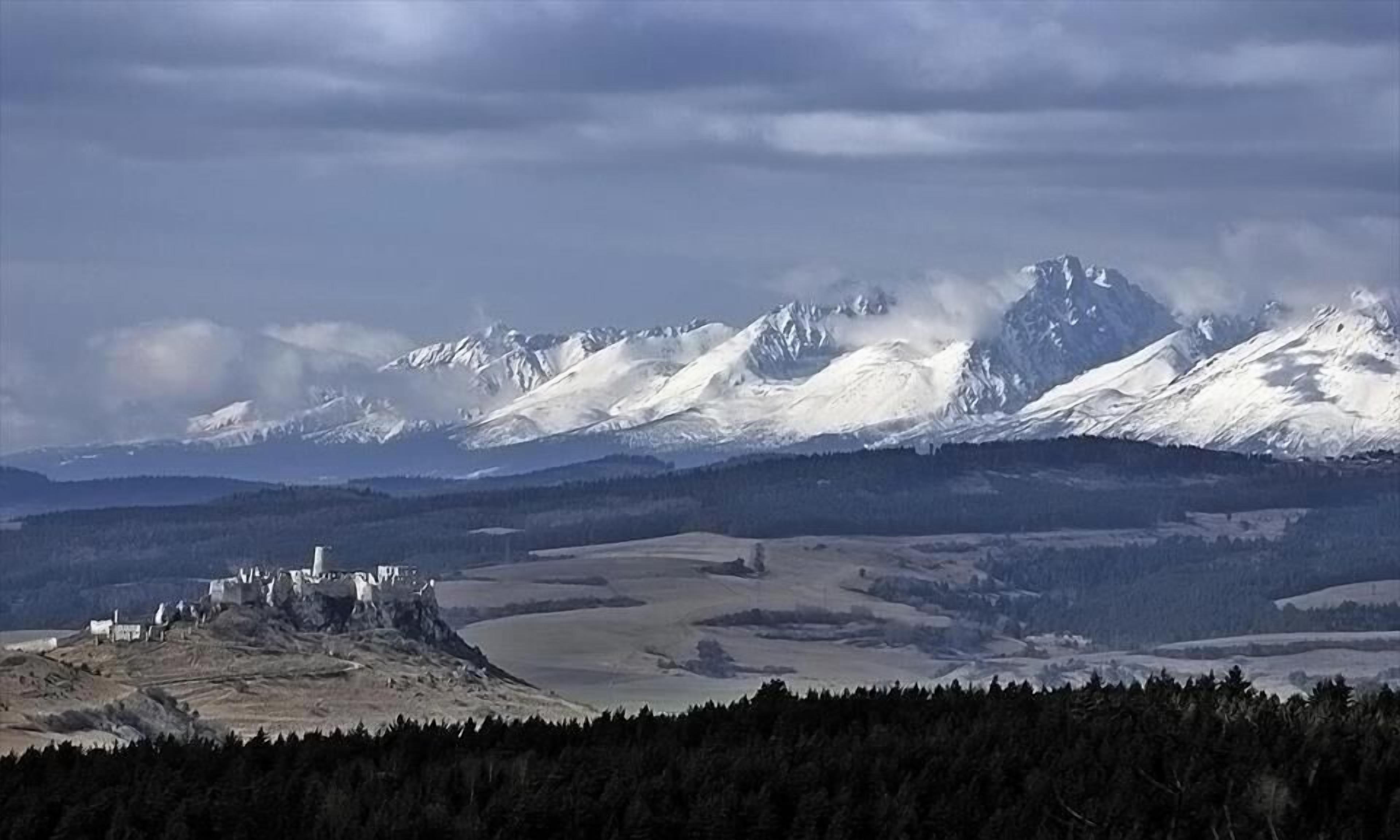 A mountainous landscape with snow-covered peaks and a castle-like structure on a hill.