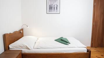 Una cama de madera con ropa blanca y un almohán verde, una lámpara de noche y un cuadro en la pared.