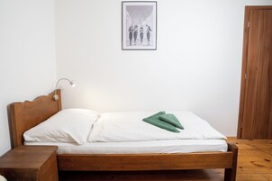 Una cama de madera con ropa blanca y un almohán verde, una lámpara de noche y un cuadro en la pared.