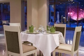 A restaurant table set with green napkins, plates, and glasses, with chairs around it.