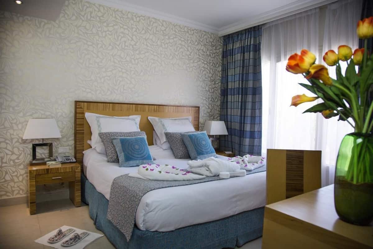 Een hotelkamer met een groot bed, twee nachtkastjes, een houten hoofdeinde en een raam met gordijnen.