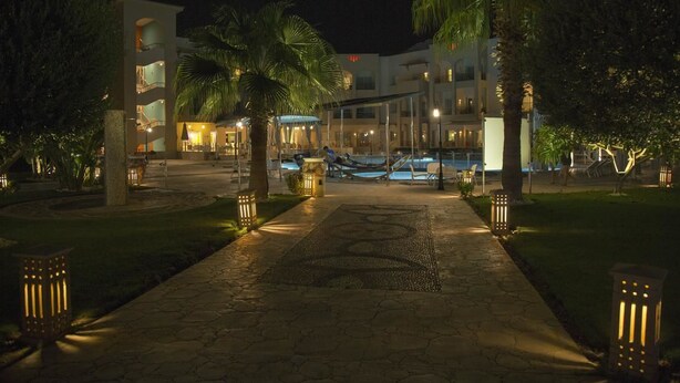 Una vista notturna di un hotel con area piscina, palme e un percorso ben illuminato.