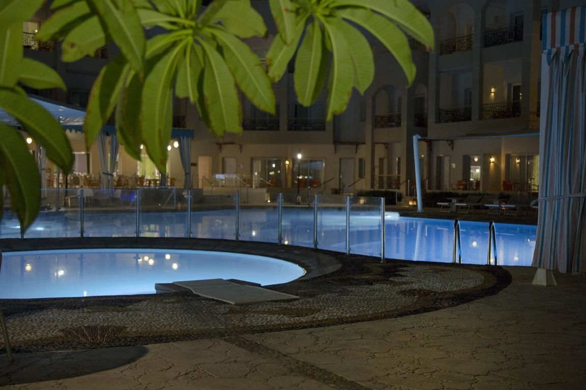 A swimming pool surrounded by a stone deck, with a building in the background.