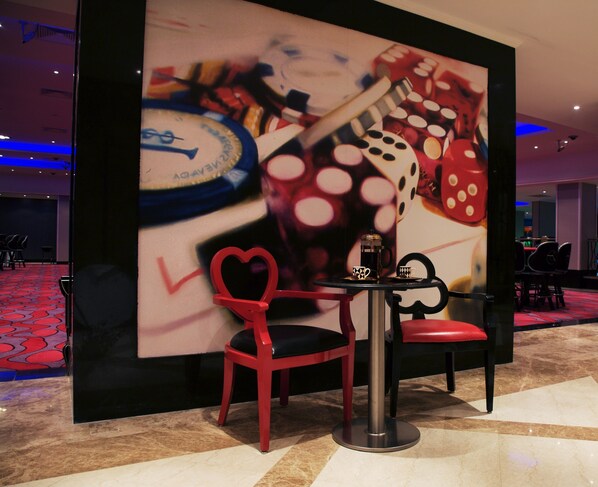 Een hotel lobby met een groot muurschilderij, een tafeltje met een koffiezetapparaat en rode stoelen.