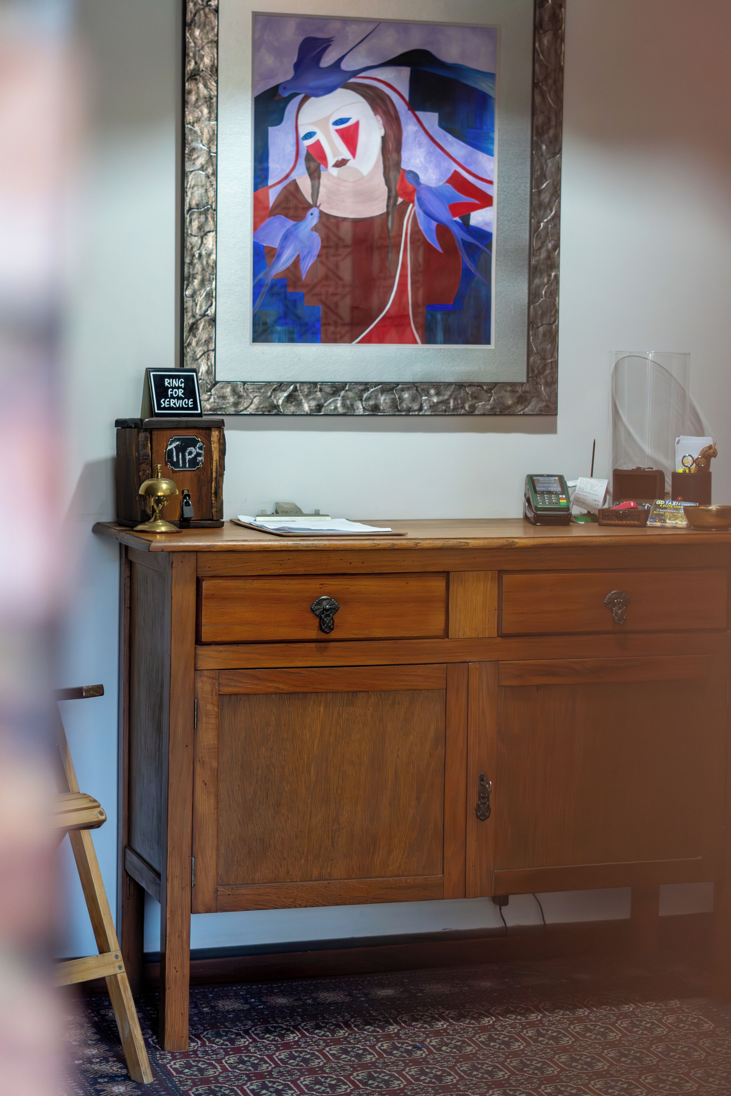Un escritorio de madera con una obra de arte enmarco, una caja registradora y un pequeño dispositivo electrónico.