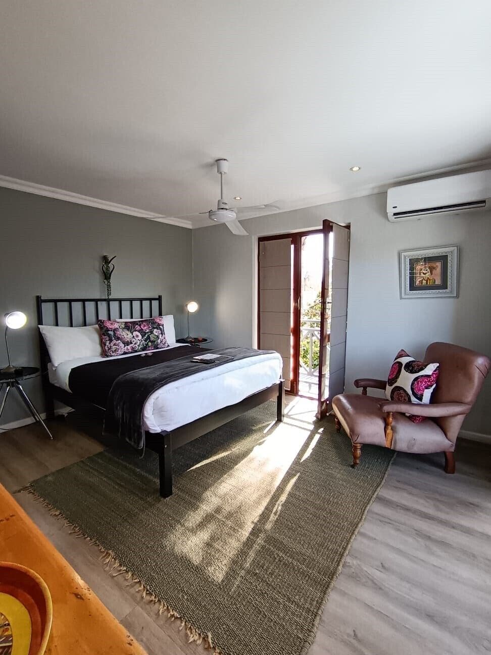 A bedroom with a bed, bedside lamps, a chair, a ceiling fan, and a door leading to a balcony.