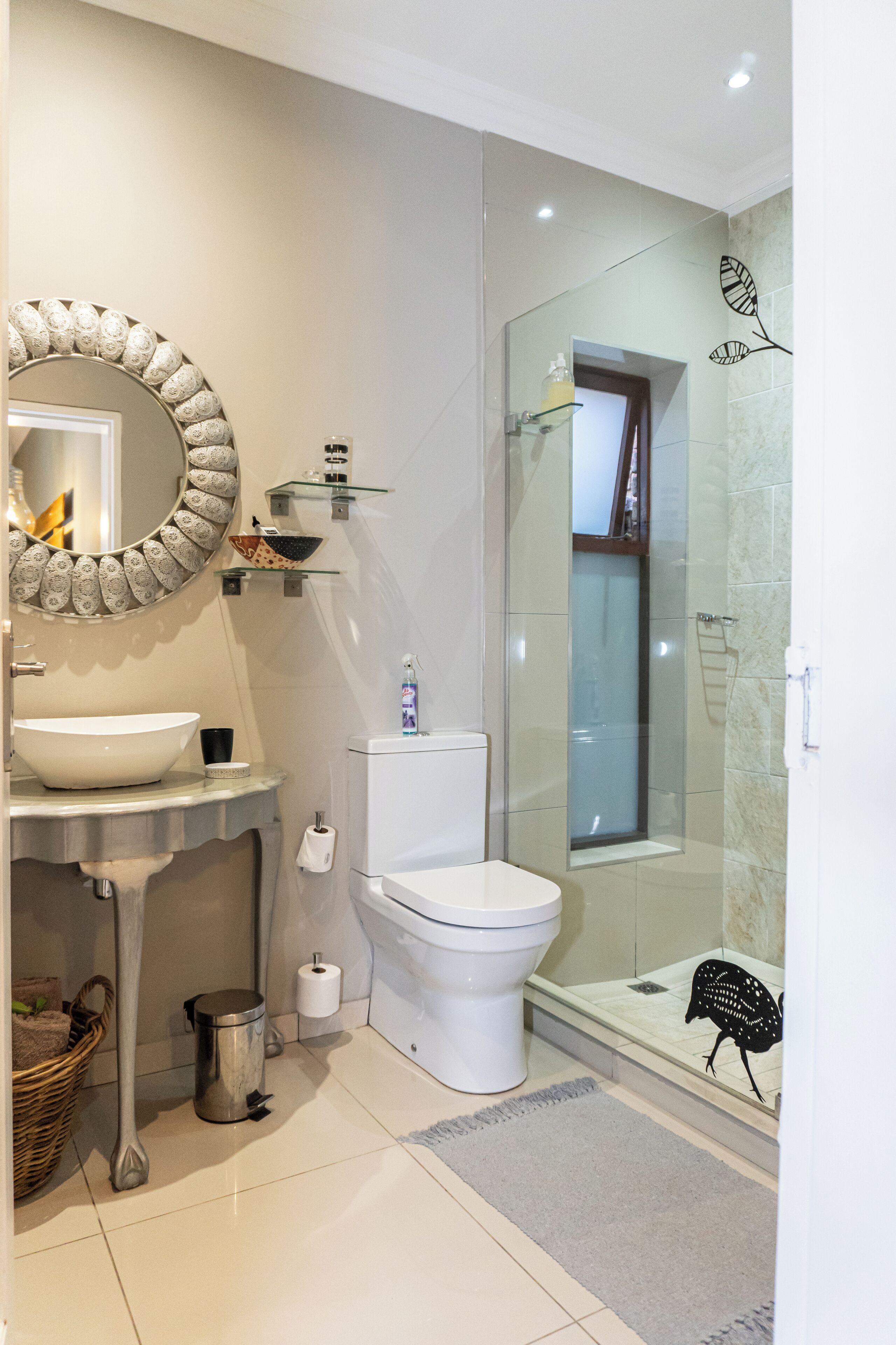 A modern bathroom with a large round mirror, a vessel sink, a toilet, and a glass-enclosed shower area.