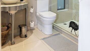 A modern bathroom with a large round mirror, a vessel sink, a toilet, and a glass-enclosed shower area.