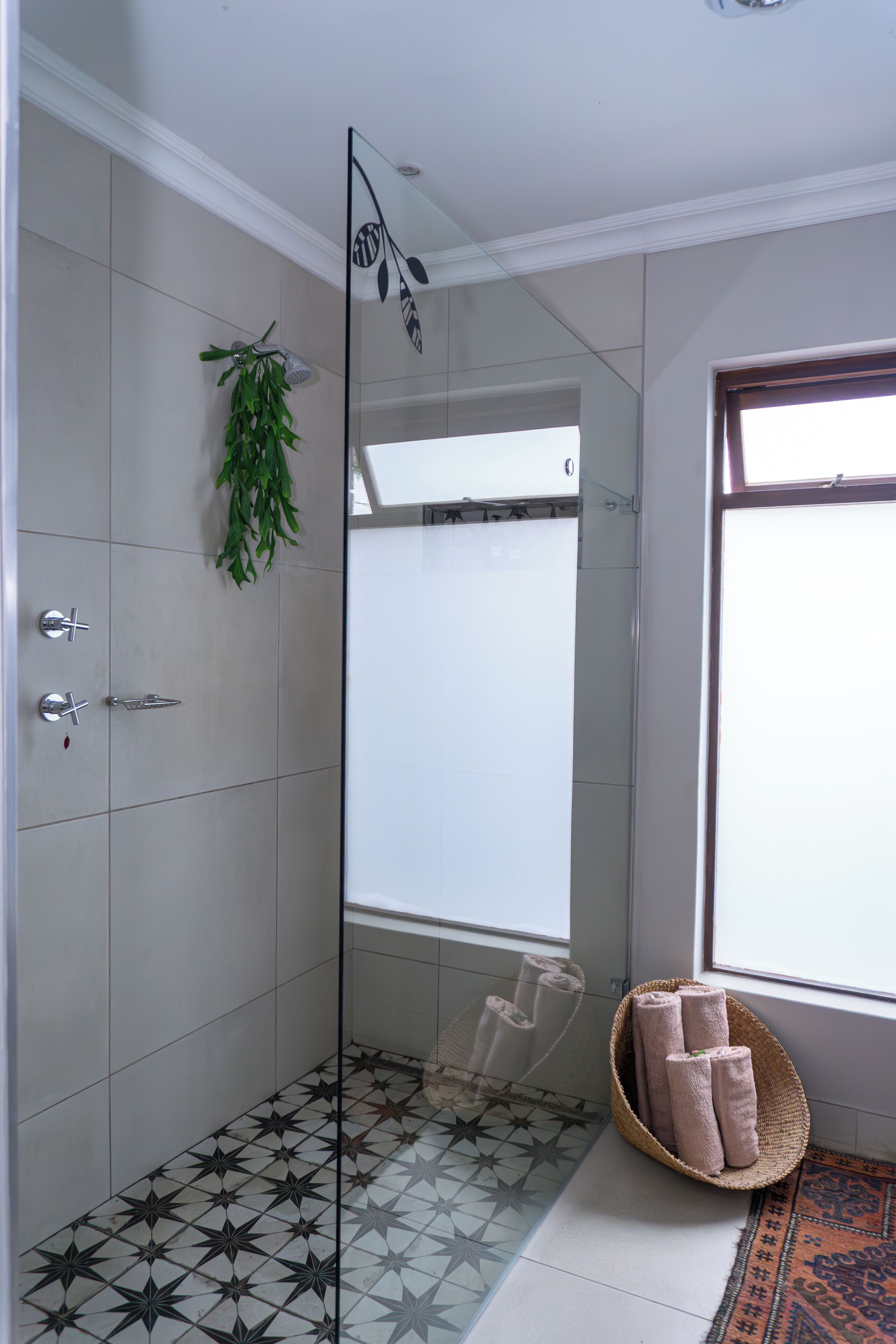 A modern bathroom with a glass shower enclosure, a hanging plant, and a woven basket with towels.