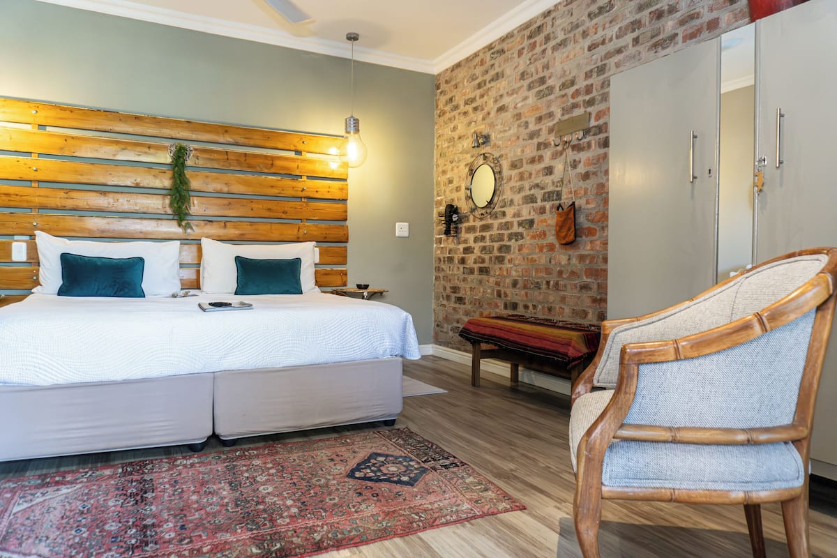 A bedroom with a bed, a wooden headboard, a brick wall, a mirror, and a wardrobe.