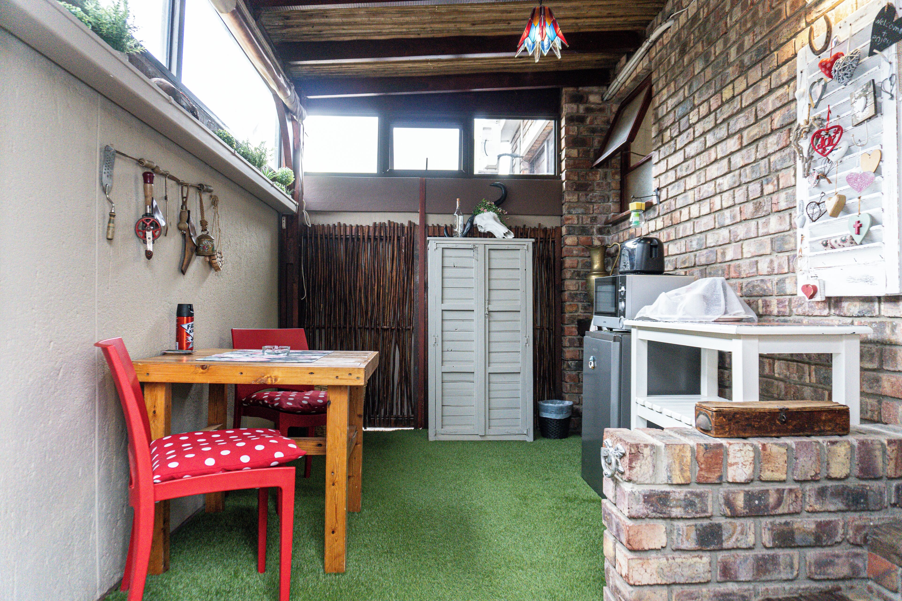 A small kitchen with a brick wall, a wooden table with red chairs, and a window above the sink.