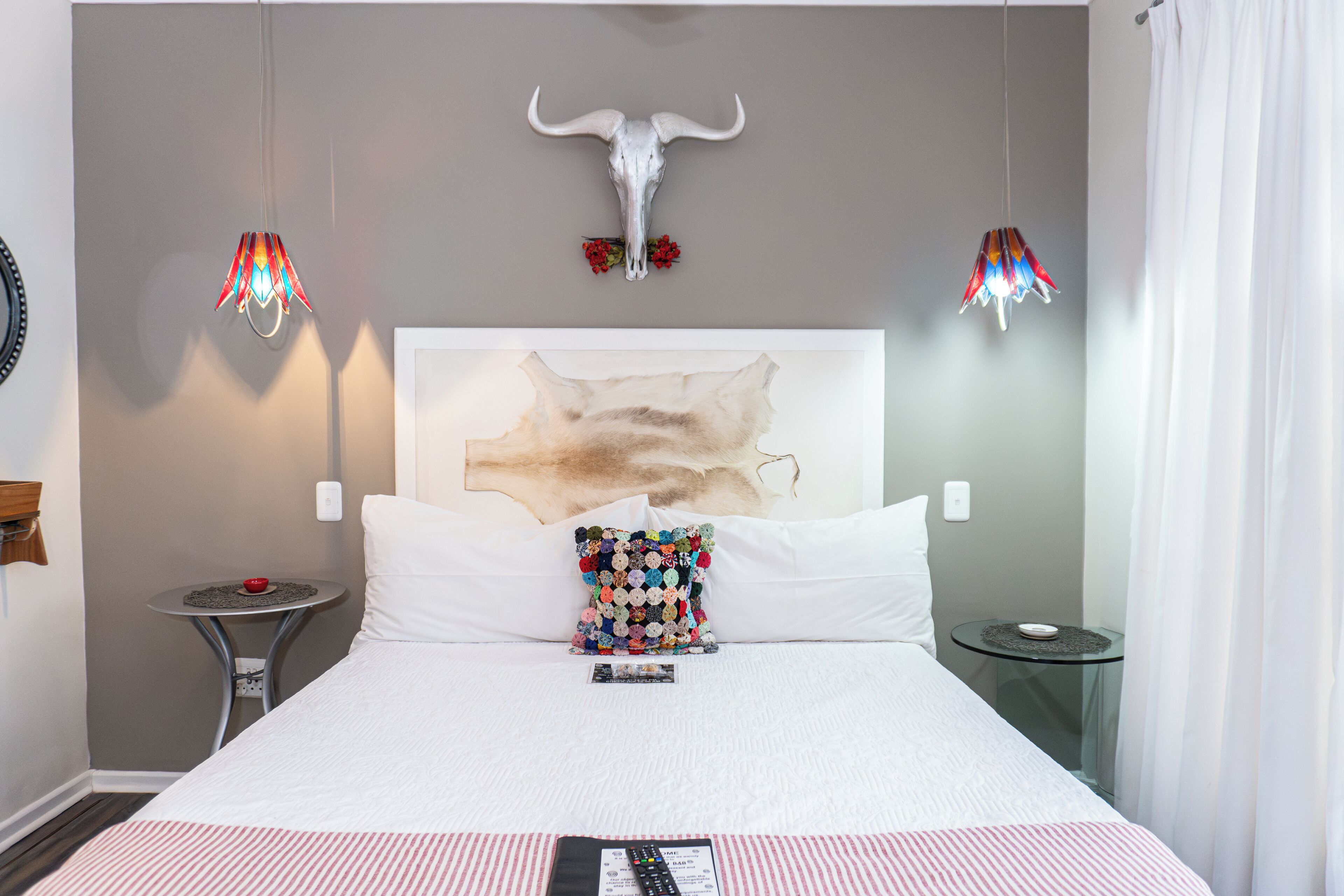 Habitación de hotel con una cama grande, un cráneo decorativo en la pared, dos mesitas auxiliares y una almohada original.
