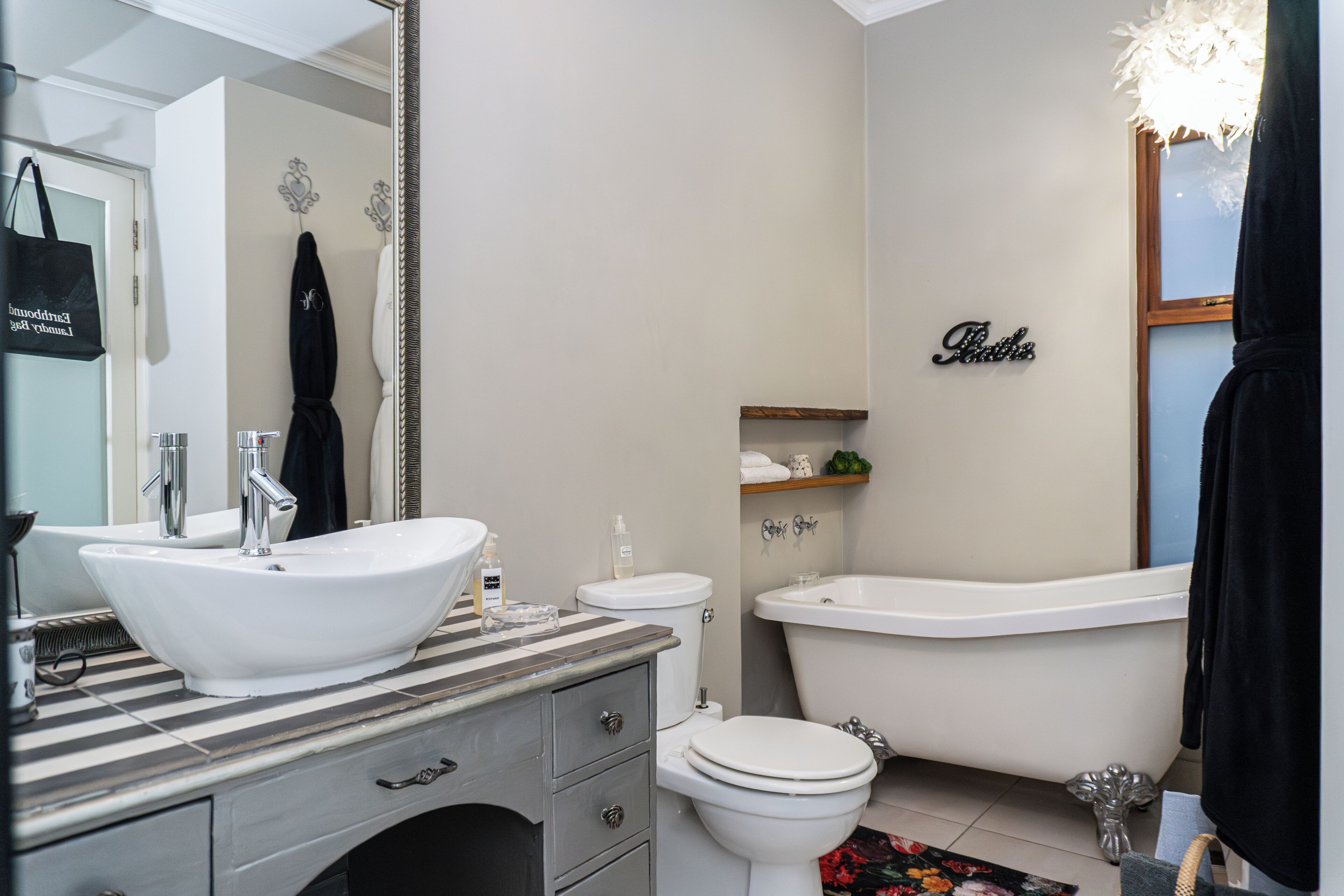 A bathroom with a white sink, toilet, and bathtub. There is a mirror, a towel rack, and a shelf with toiletries.