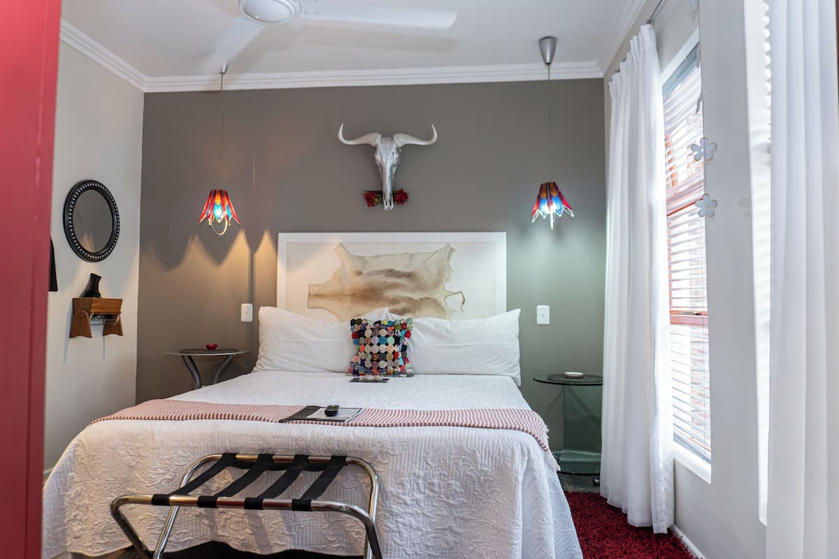 A bedroom with a bed, a headboard with a cow skull, a hanging light fixture, and a window with blinds.