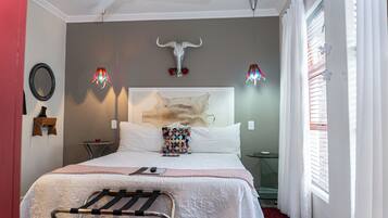 A bedroom with a bed, a headboard with a cow skull, a hanging light fixture, and a window with blinds.