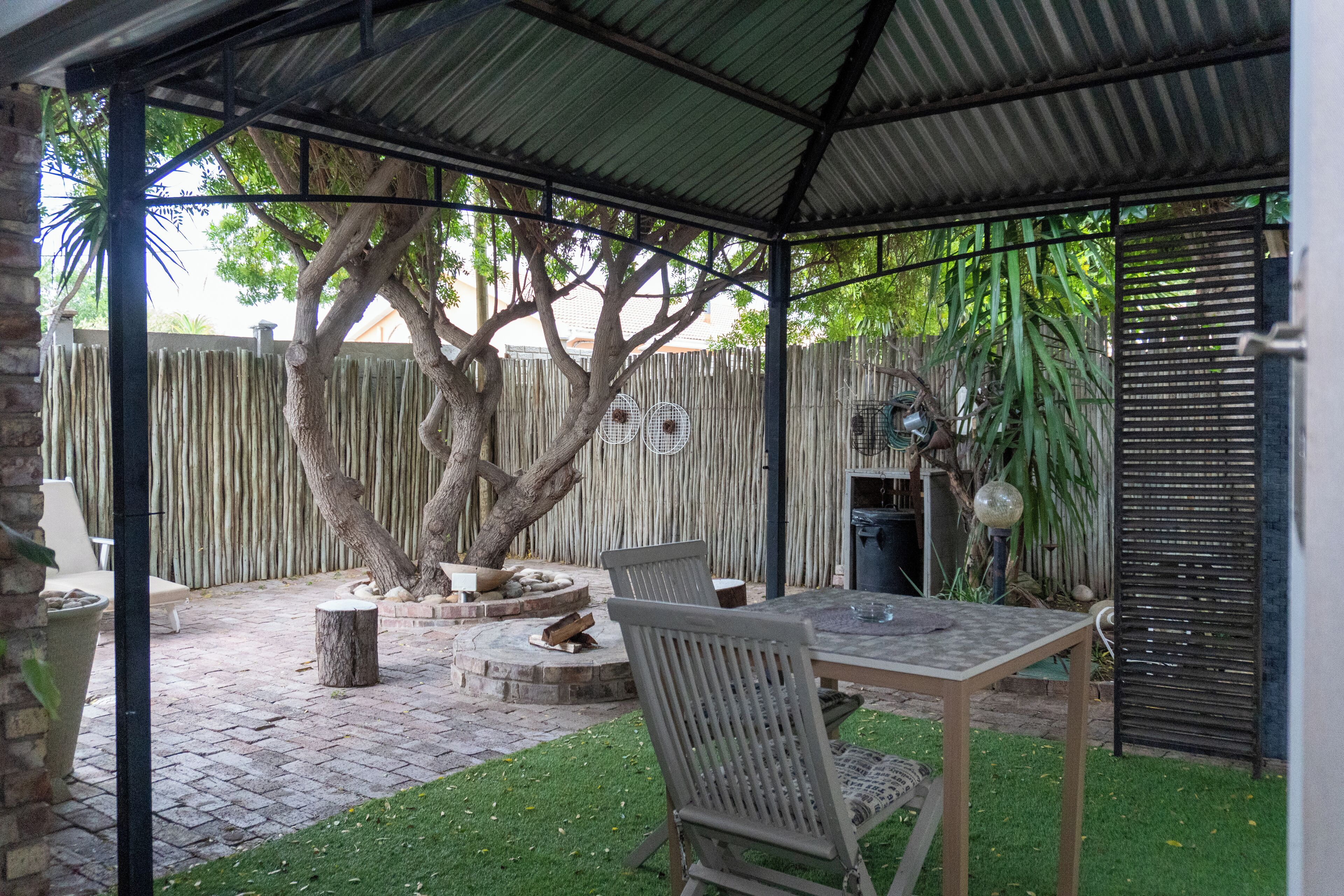 Un porche cubierto con una mesa y sillas, rodeado por una valla de madera y árboles.
