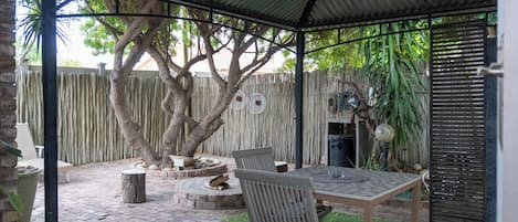 Un porche cubierto con una mesa y sillas, rodeado por una valla de madera y árboles.