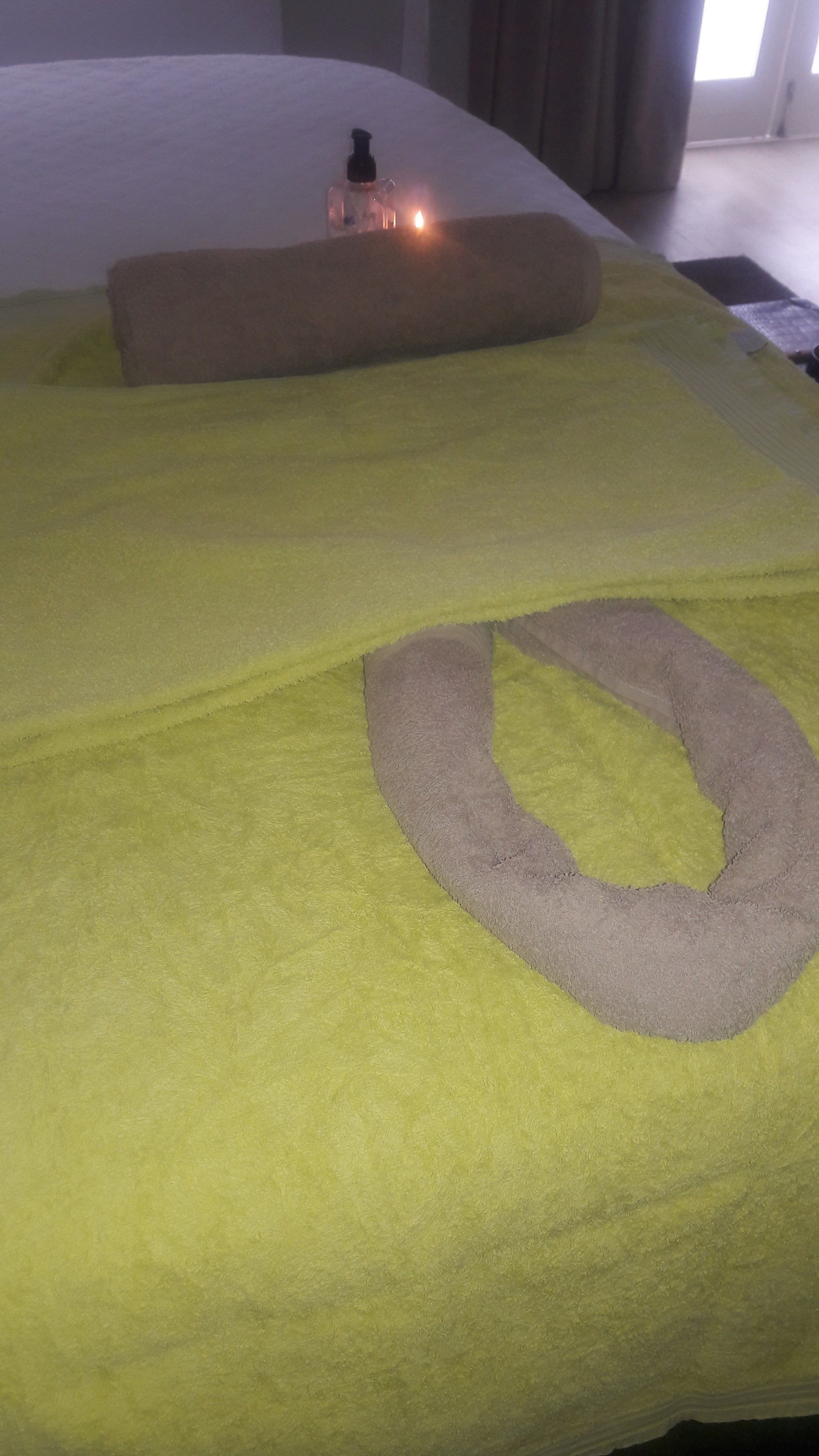 A bed with a green blanket, a brown pillow, and a bottle of lotion on it.