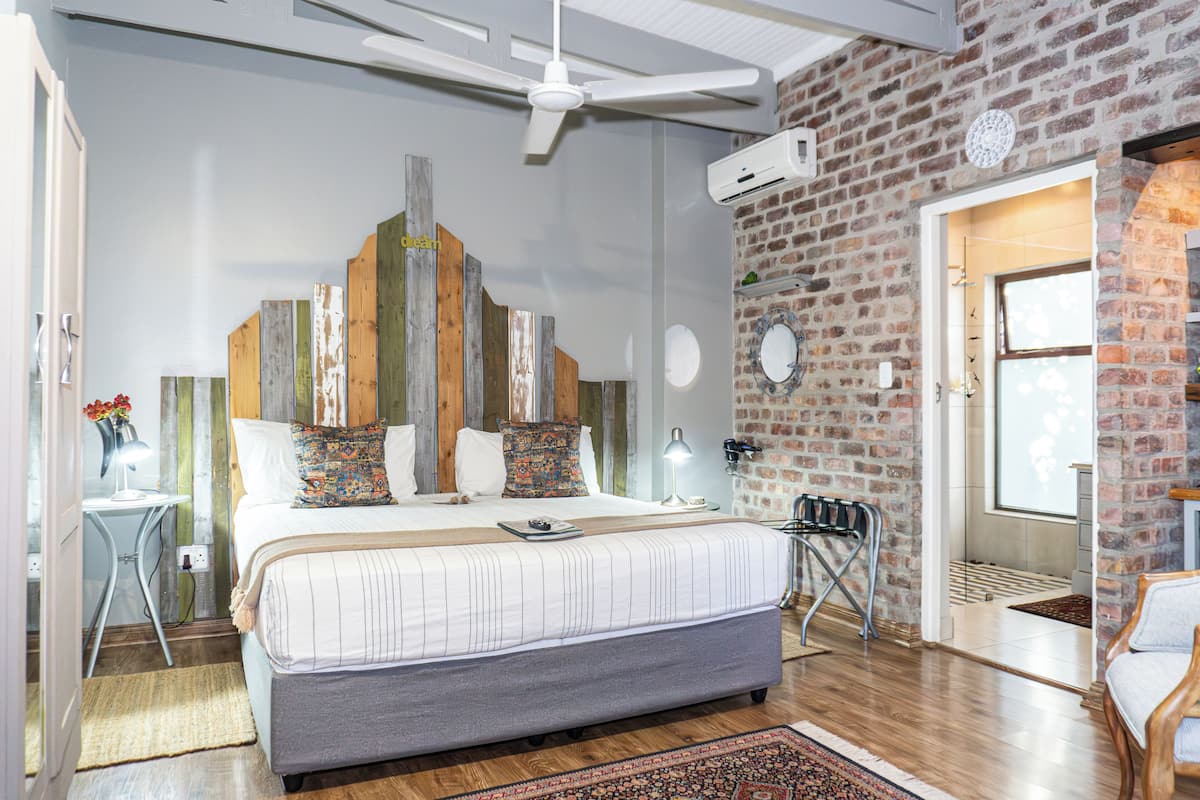 A bedroom with a large bed, a ceiling fan, a brick wall, and a door leading to another room.